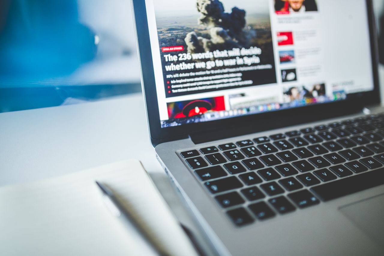 about-us Open laptop displaying an online news article on a desk with a notebook nearby.
