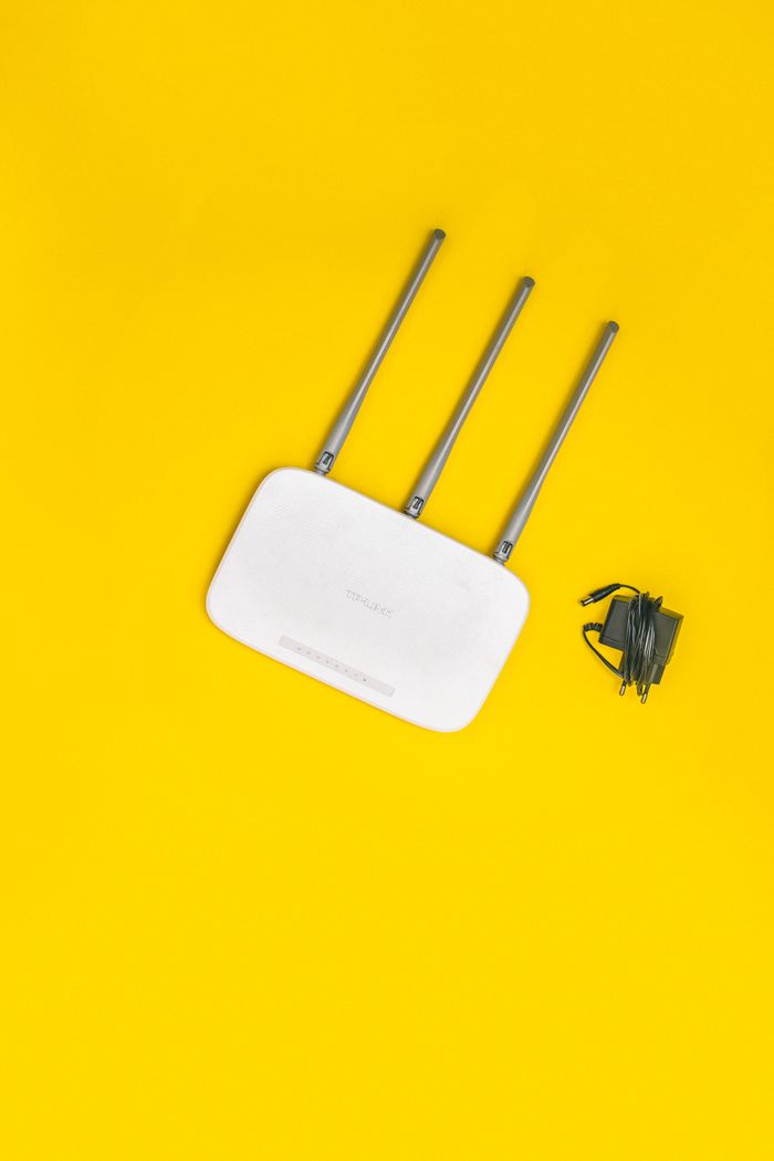 services-01 White router with three antennas and cables on bold yellow background, ideal for tech concepts.